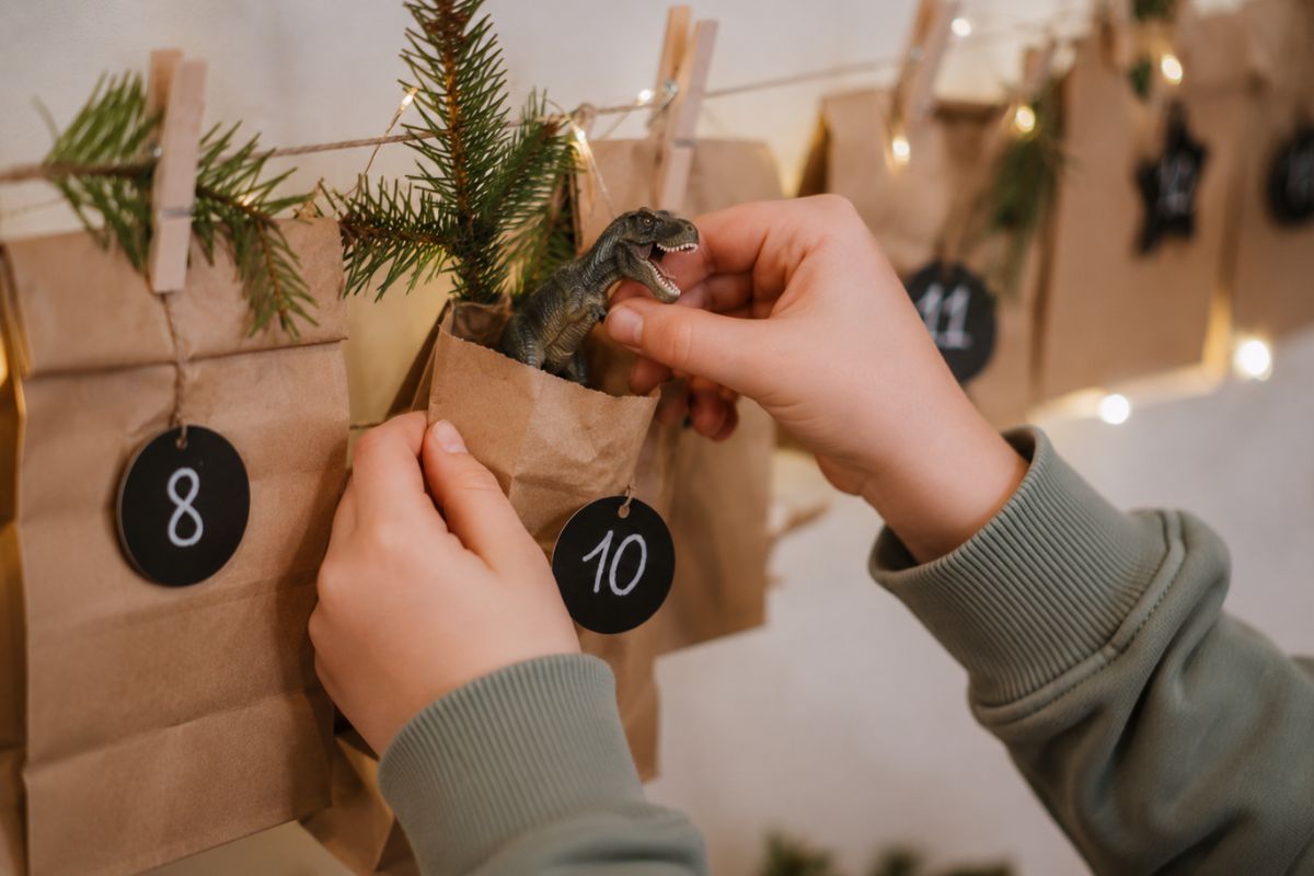 Kind zieht eine kleine Dinosaurierfigur aus einer nummerierten Papiertüte eines selbst befüllten Adventskalenders.