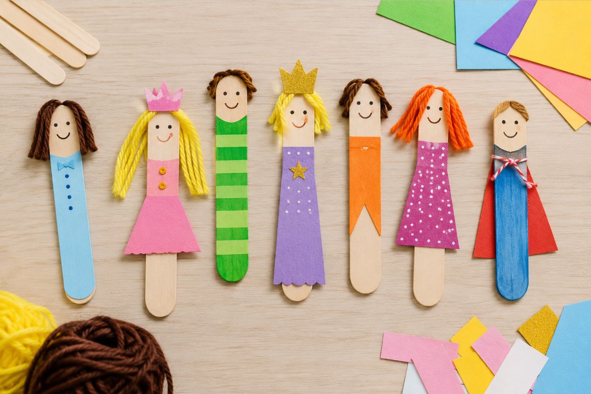 Bunte Figuren aus Eisstielen und Holzstäbchen mit Gesichtern, Wolle und Papierkleidung als einfache Bastelidee für Kinder.