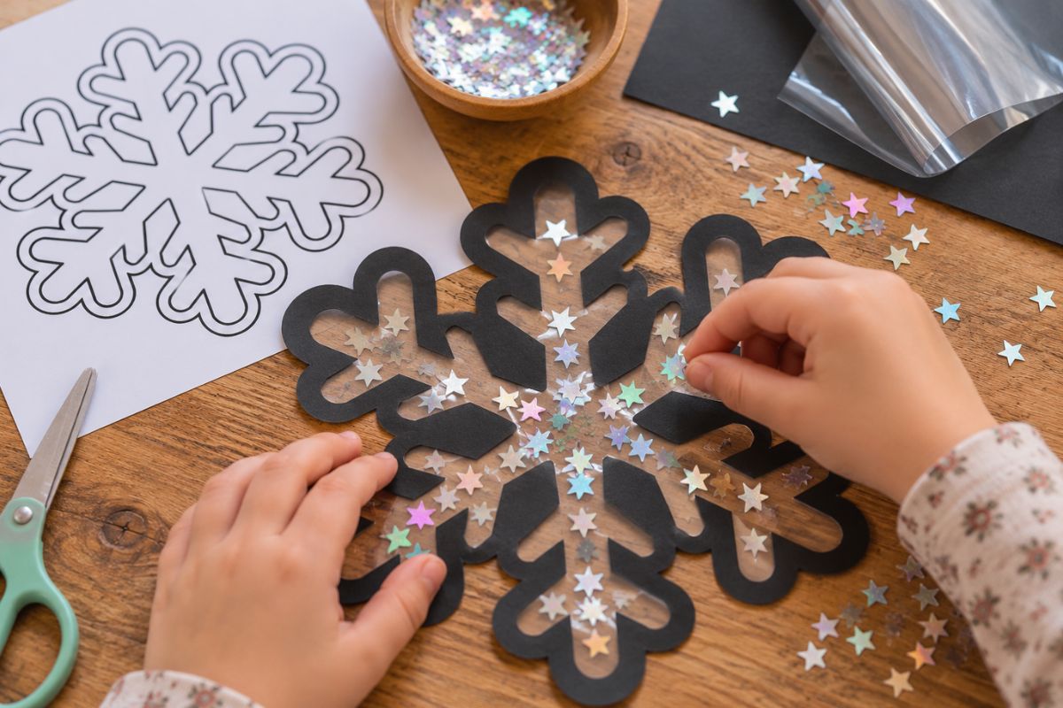 Fensterbild zu Weihnachten basteln: Schneeflocke aus Tonkarton mit transparenter Folie und Glitzersternen