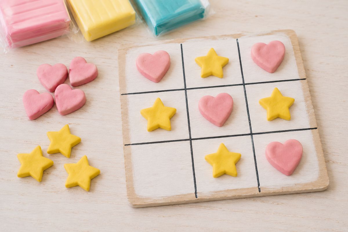 Selbstgemachtes Tic-Tac-Toe-Spiel aus Fimo mit Herzen und Sternen als Spielsteine auf einem Holzbrett für Kinder