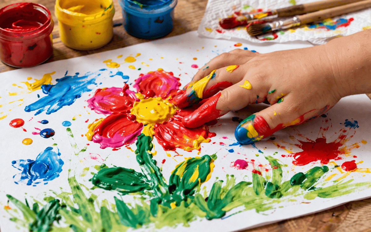 Kind malt mit Fingerfarben einfache bunte Blumen auf Papier.