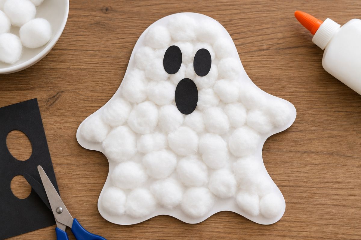 Gespenst aus Wattebällchen mit schwarzen Augen und Mund auf weißem Papier – einfache Halloween-Bastelidee für Kinder.