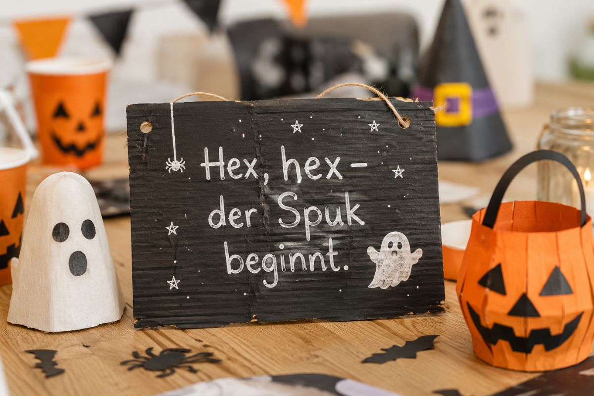 Selbst gebasteltes Halloween-Dekoschild mit dem Spruch „Hex, hex – der Spuk beginnt.“ auf einem festlich dekorierten Partytisch mit Kürbislaterne, Gespenst und Halloween-Dekoration.