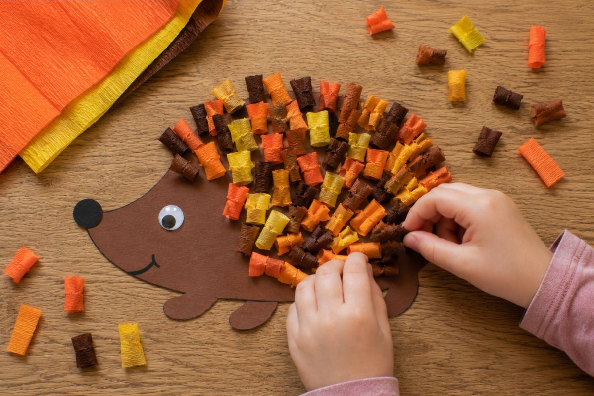 Igel basteln mit Krepppapier: Von einem Kind gestalteter Igel aus braunem Tonpapier mit kurzen eingedrehten Krepppapierstreifen als bunte Stacheln