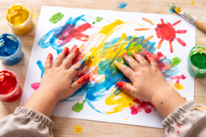 Kind 3 Jahre bastelt mit Fingerfarben und gestaltet ein buntes Bild