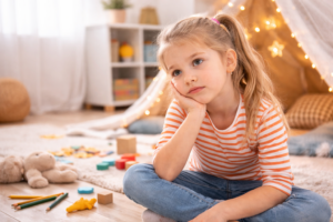 7 jähriges Mädchen sitzt gelangweilt in ihrem Zimmer am Tisch und weiß nicht, was sie tun soll