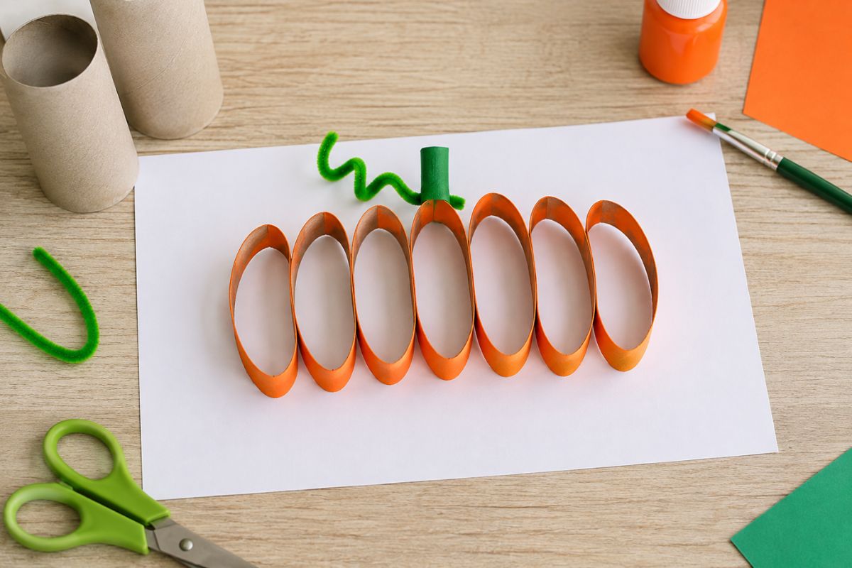 Halloween-Kürbis aus gleich großen Ringen einer Klopapierrolle auf weißem Papier – einfache Bastelidee für Kinder.