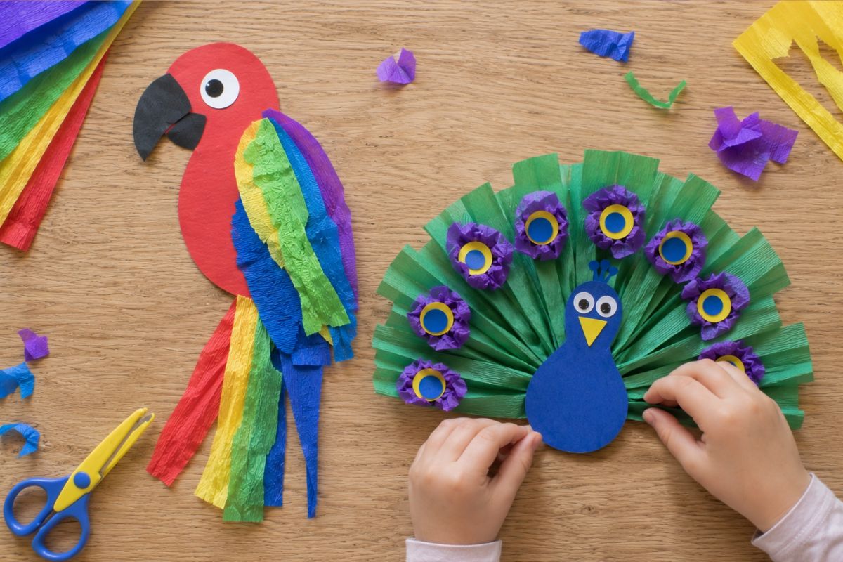 Papagei und Pfau basteln mit Krepppapier: Von einem Kind gestalteter Papagei mit gerissenen Krepppapierstreifen als Federn sowie Pfau mit fächerförmigem Schwanz aus gerafften Krepppapierstreifen und bunten Papierkreisen