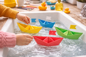 Kinder testen gefaltete Papierboote im Waschbecken und beobachten welche Boote am besten schwimmen