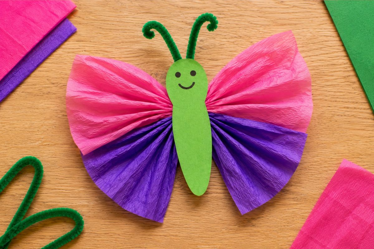 Schmetterling basteln mit Krepppapier: Von einem Kind gebastelter Schmetterling mit gerafften Krepppapierflügeln, grünem Tonpapierkörper und Pfeifenreiniger-Fühlern
