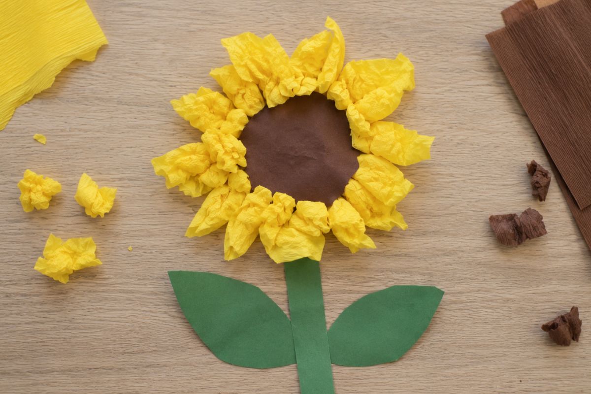 Sonnenblume basteln mit Krepppapier: Von einem Kind gebastelte Sonnenblume aus geknülltem gelbem Krepppapier sowie grünem und braunem Tonpapier.