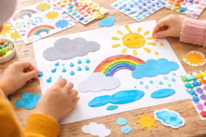 Kinder gestalten ein Wetterbild mit Stickern, Regenbogen, Wolken und Regentropfen auf Papier