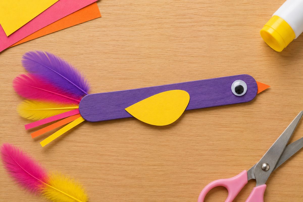 Selbst gebastelter Vogel aus einem bemalten Holzstäbchen mit Papierflügel, Wackelauge, Papierschnabel und bunten Federn als einfache Bastelidee für Kinder.