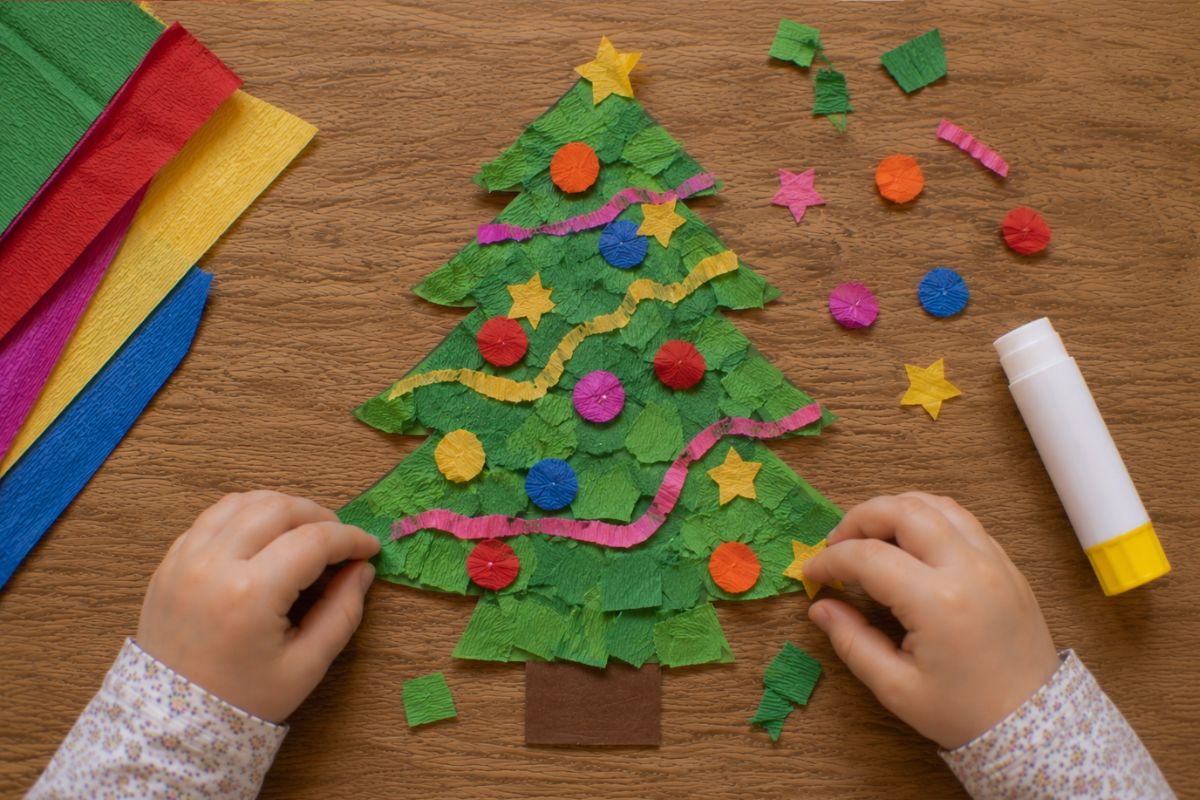 Weihnachtsbaum basteln mit Krepppapier: Von einem Kind gestalteter Tannenbaum aus grünem Tonpapier mit gerissenen Krepppapierstücken sowie bunten Kugeln, Sternen und Lametta aus Krepppapier